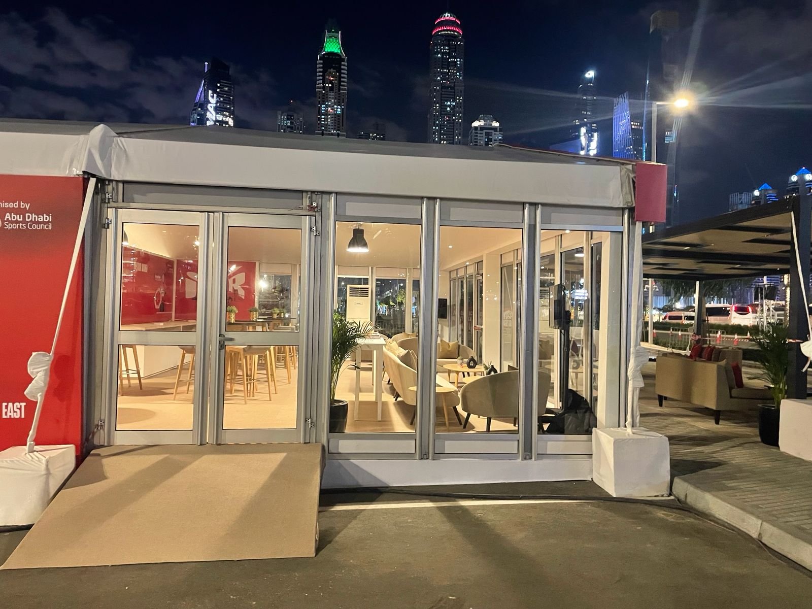 Glass-fronted VIP event tent lit up at night with the Abu Dhabi skyline behind