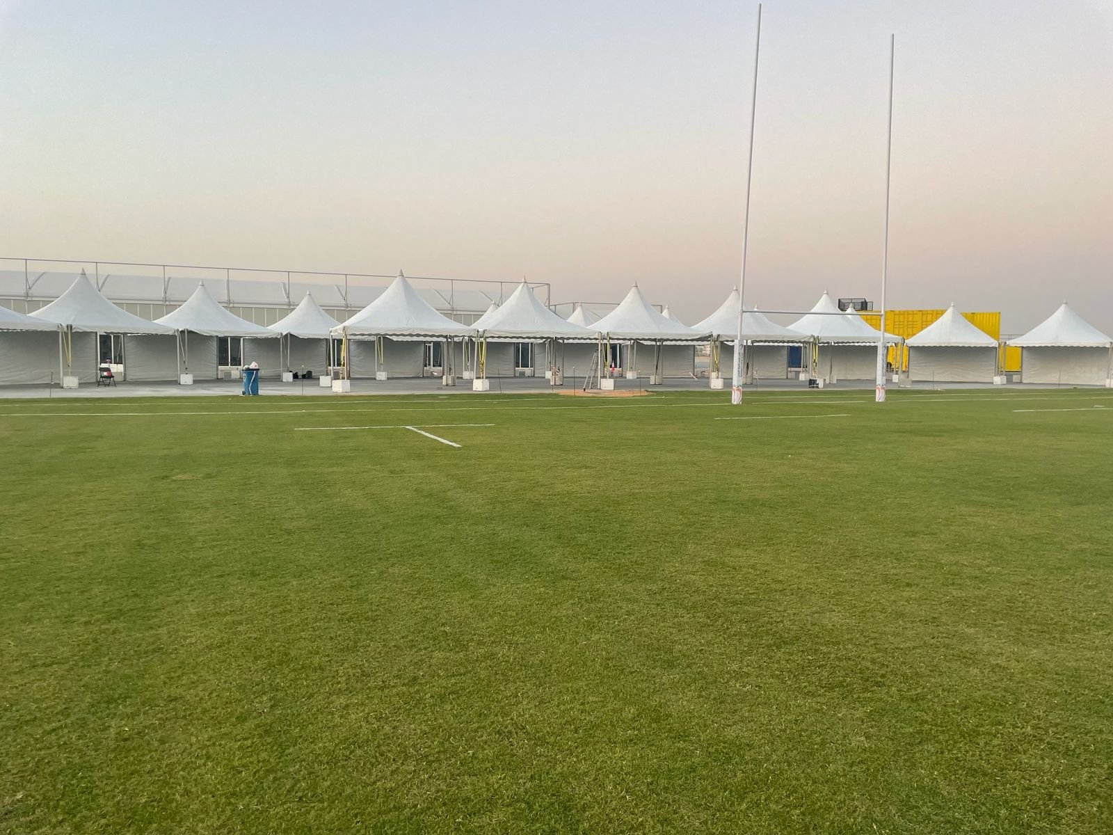 Line of pagoda tents at dusk beside a sports pitch